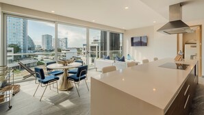 A modern kitchen with a large island, dining area with blue chairs, and large windows offering city views. - Modern apartment in Puerto Cancun with partial ocean and marina view 🌊 (Puerto Cancun)
