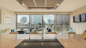 A modern hotel room with a large window offering a city view, a flat-screen TV, and a dining area with a table and chairs. - Modern apartment in Puerto Cancun with partial ocean and marina view 🌊 (Puerto Cancun)