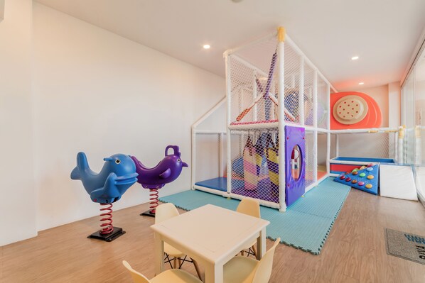 A play area with a climbing structure, a table with chairs, and a colorful play mat.