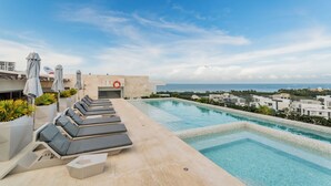 A rooftop pool area with lounge chairs, umbrellas, and a lifebuoy. - Modern apartment in Puerto Cancun with partial ocean and marina view 🌊 (Puerto Cancun)