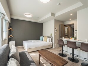 A modern hotel room with a bed, a sofa, a bench, a desk with two chairs, and a bathroom with a mirror. - ESLEAD HOTEL Namba Dotonbori East (Osaka)