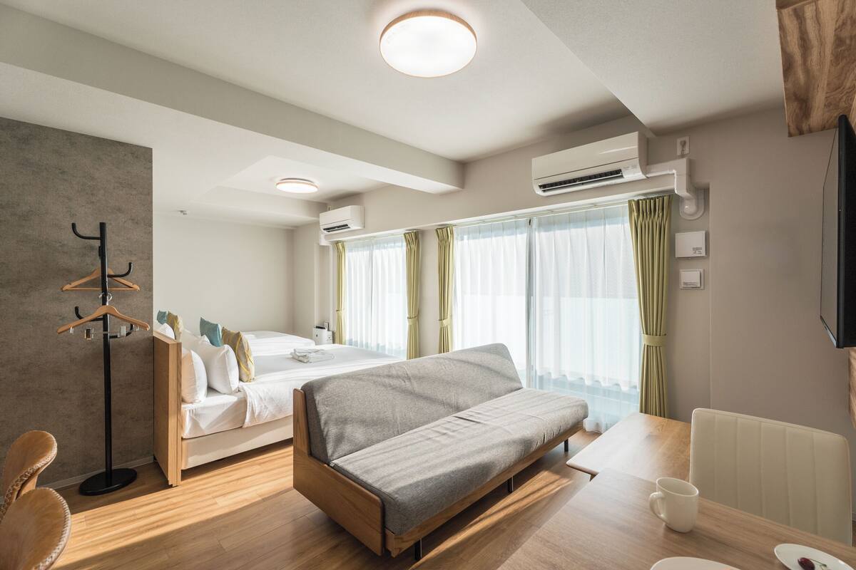 A modern hotel room with a sofa, a bed, a dining table, and a coat rack.