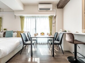 A modern hotel room with a bed, a dining table with chairs, an air conditioning unit, and a window with curtains. - ESLEAD HOTEL Namba Dotonbori East (Osaka)