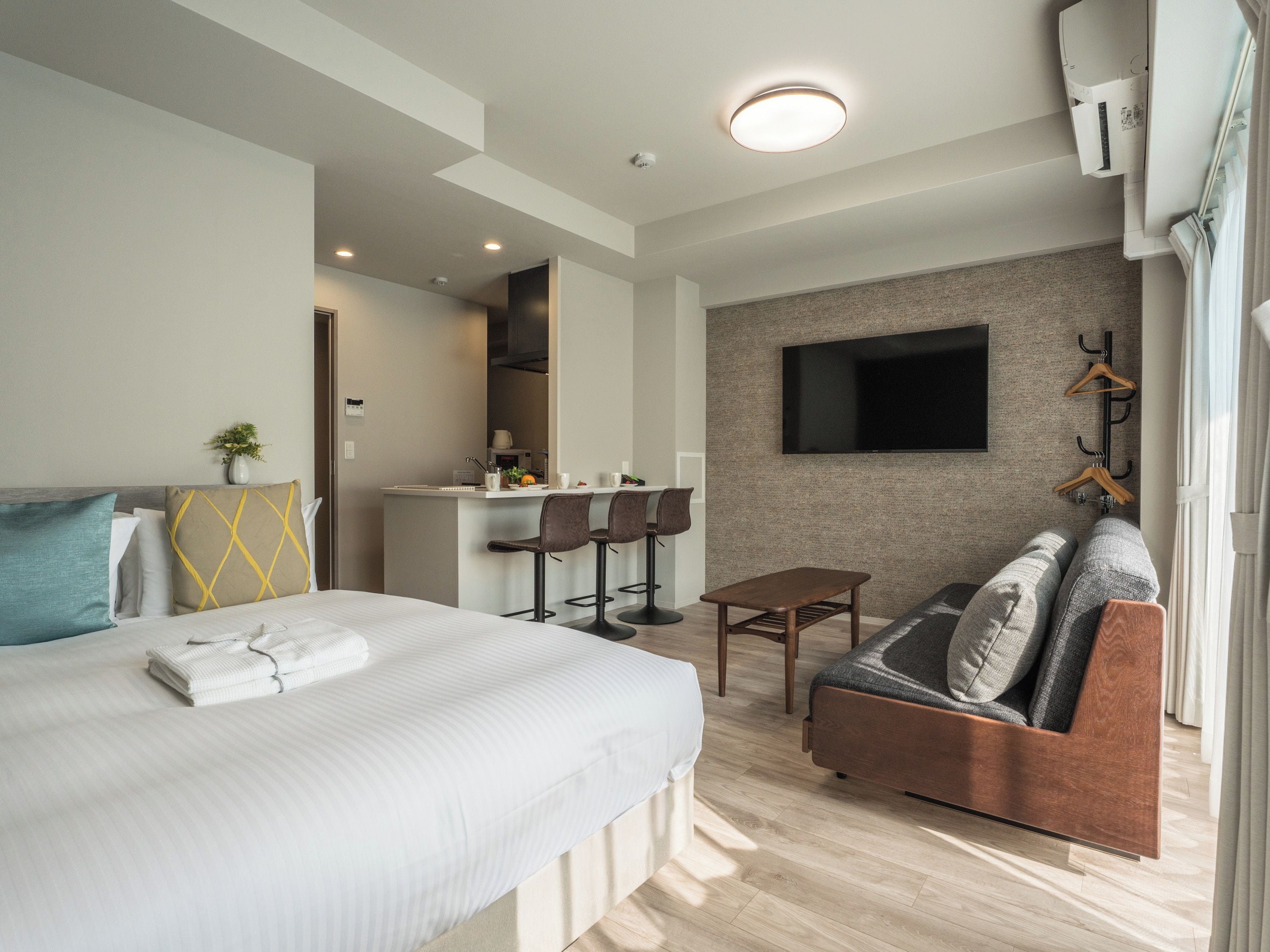 Habitación de hotel con cama, sofá, una mesita, televisor montado en la pared y una zona de kitchenette.
