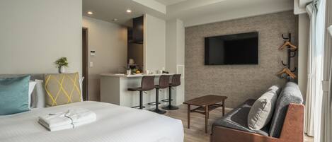 Habitación de hotel con cama, sofá, una mesita, televisor montado en la pared y una zona de kitchenette.