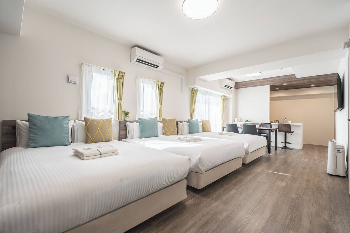 A hotel room with three beds, a desk, and a kitchenette.