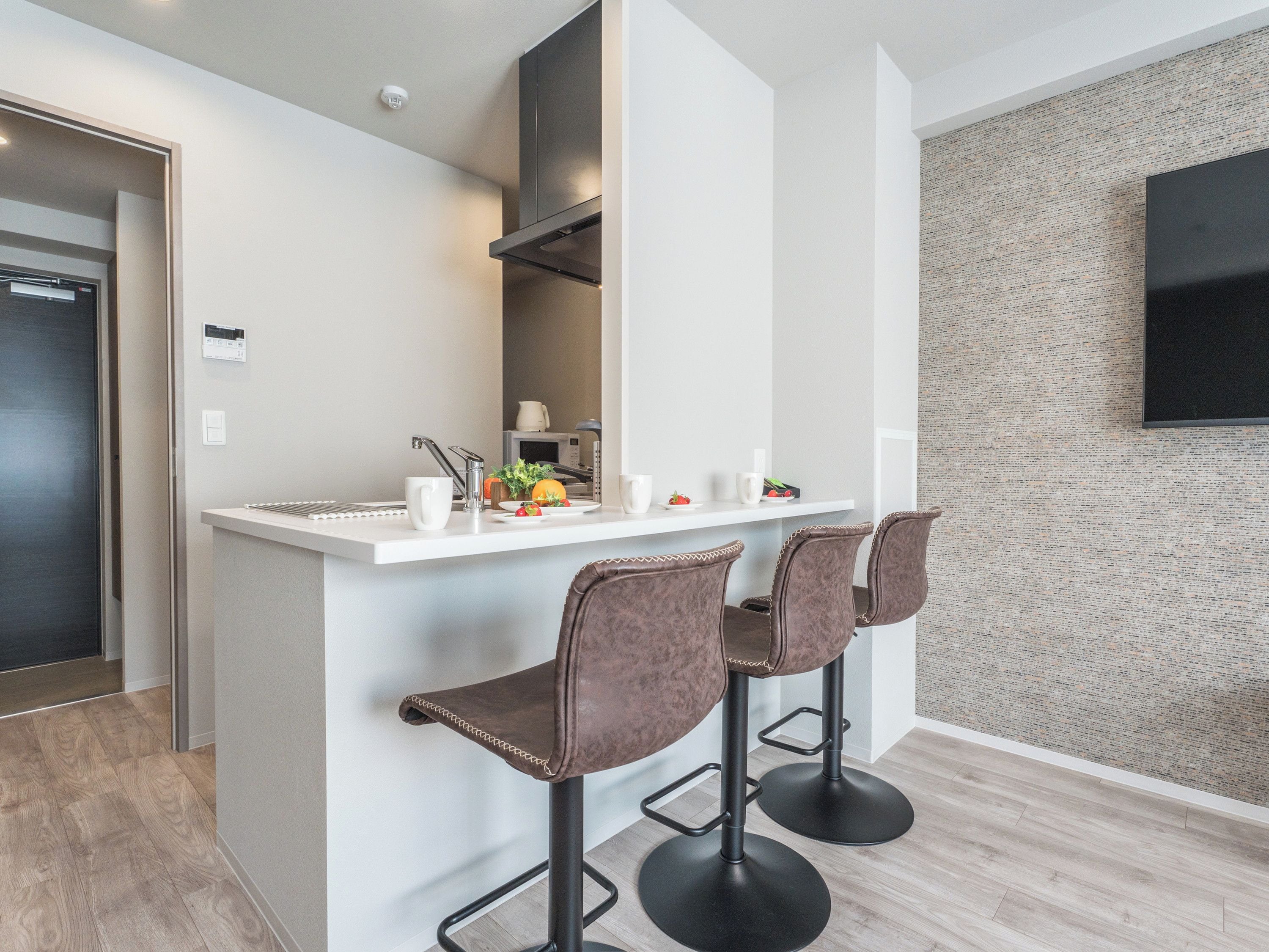 A modern kitchen with a white countertop, two bar stools, and a wall-mounted TV.