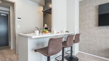 A modern kitchen with a white countertop, two bar stools, and a wall-mounted TV.