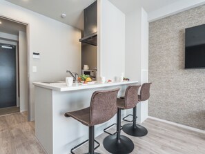 A modern kitchen with a white countertop, two bar stools, and a wall-mounted TV.