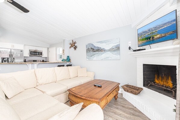 Ett vardagsrum med en vit soffa, ett soffbord i trä, en öppen spis och en tv som är monterad ovanför den.