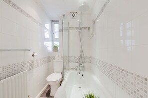 A bathroom with a bathtub, toilet, and shower. - GuestReady - Charming Retreat in Vibrant London (London)