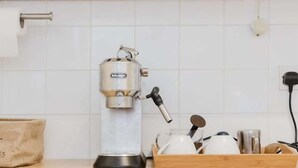 A kitchen with white cabinets, a coffee maker, and wooden stools. - GuestReady - Charming Retreat in Vibrant London (London)