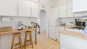 A modern kitchen with white cabinets, a wooden countertop, a gas stove, a microwave, and a coffee machine. - GuestReady - Charming Retreat in Vibrant London (London)
