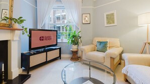 A modern living room with a flat-screen TV, a sofa, a glass coffee table, and a fireplace. - GuestReady - Charming Retreat in Vibrant London (London)