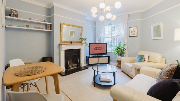 A modern living room with a fireplace, a television, a sofa, a coffee table, and a dining area. - GuestReady - Charming Retreat in Vibrant London (London)