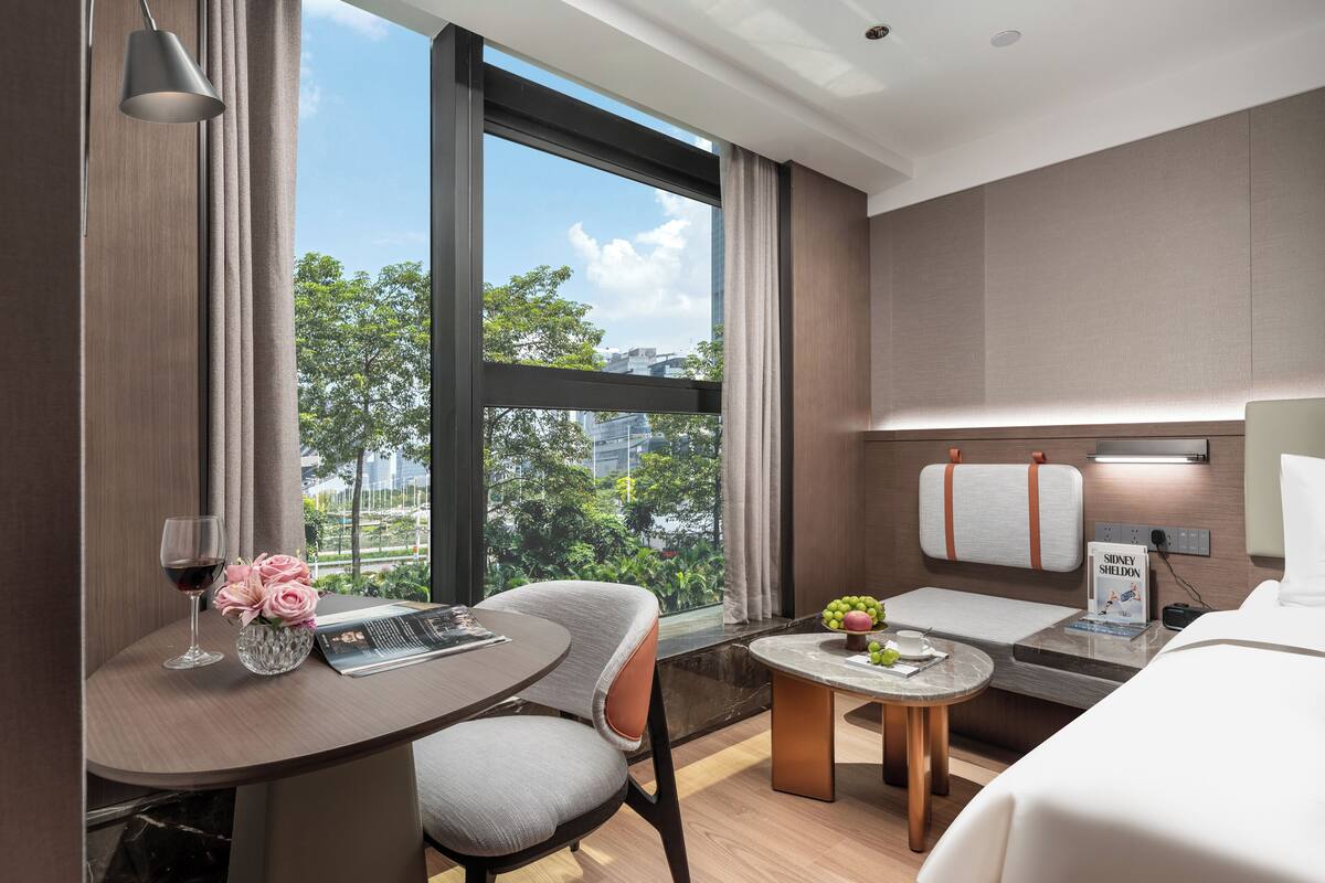 Una habitación de hotel moderna con comedor, cama y vistas a zonas verdes.