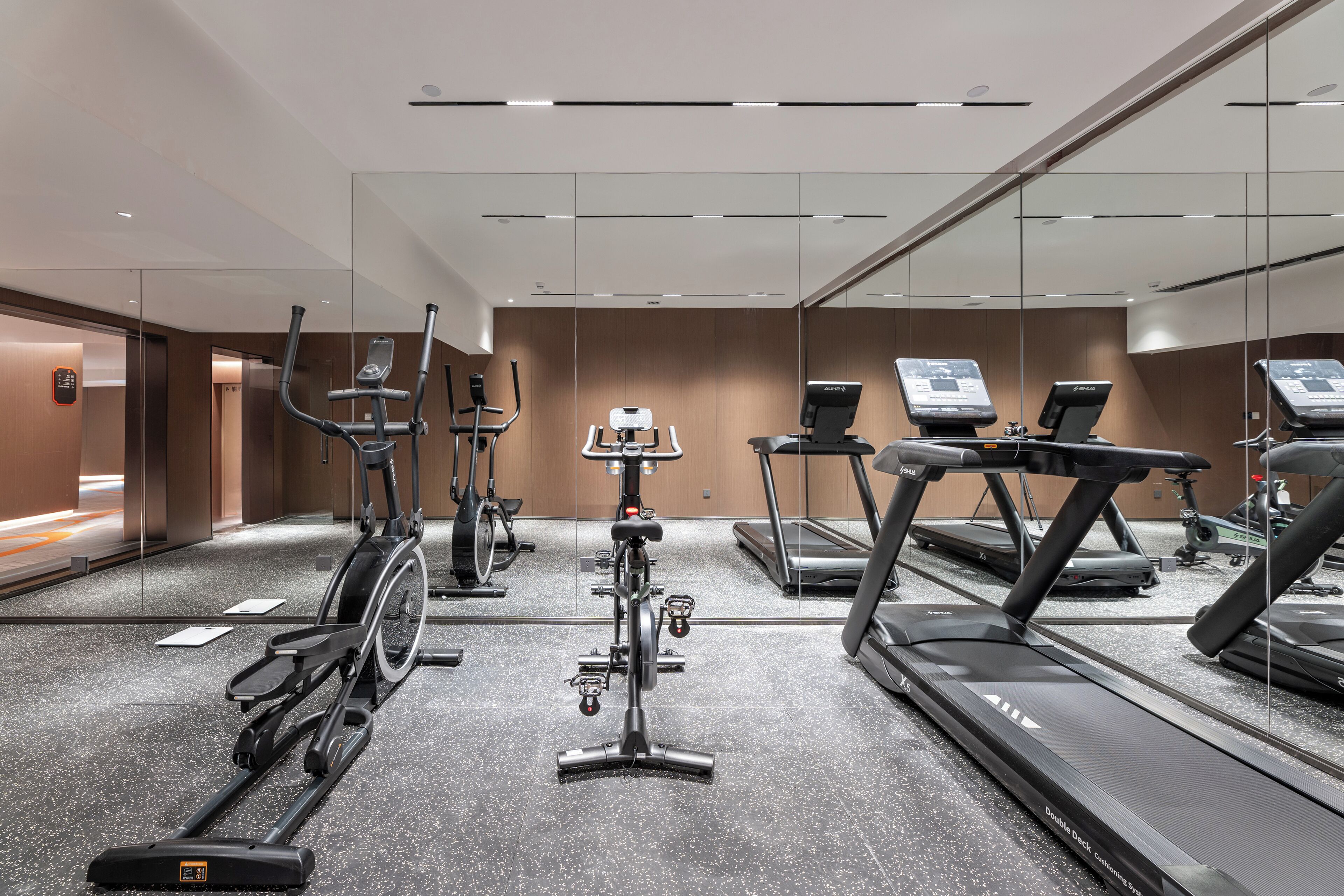 Un gimnasio moderno con diversas máquinas de cardio, un espejo grande y un ambiente limpio y bien iluminado.