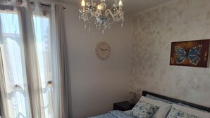 A bedroom with a bed, a chandelier, a clock, and a butterfly painting.