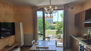 A compact kitchen with a dining area, a TV mounted on the wall, and a view of the outside balcony.