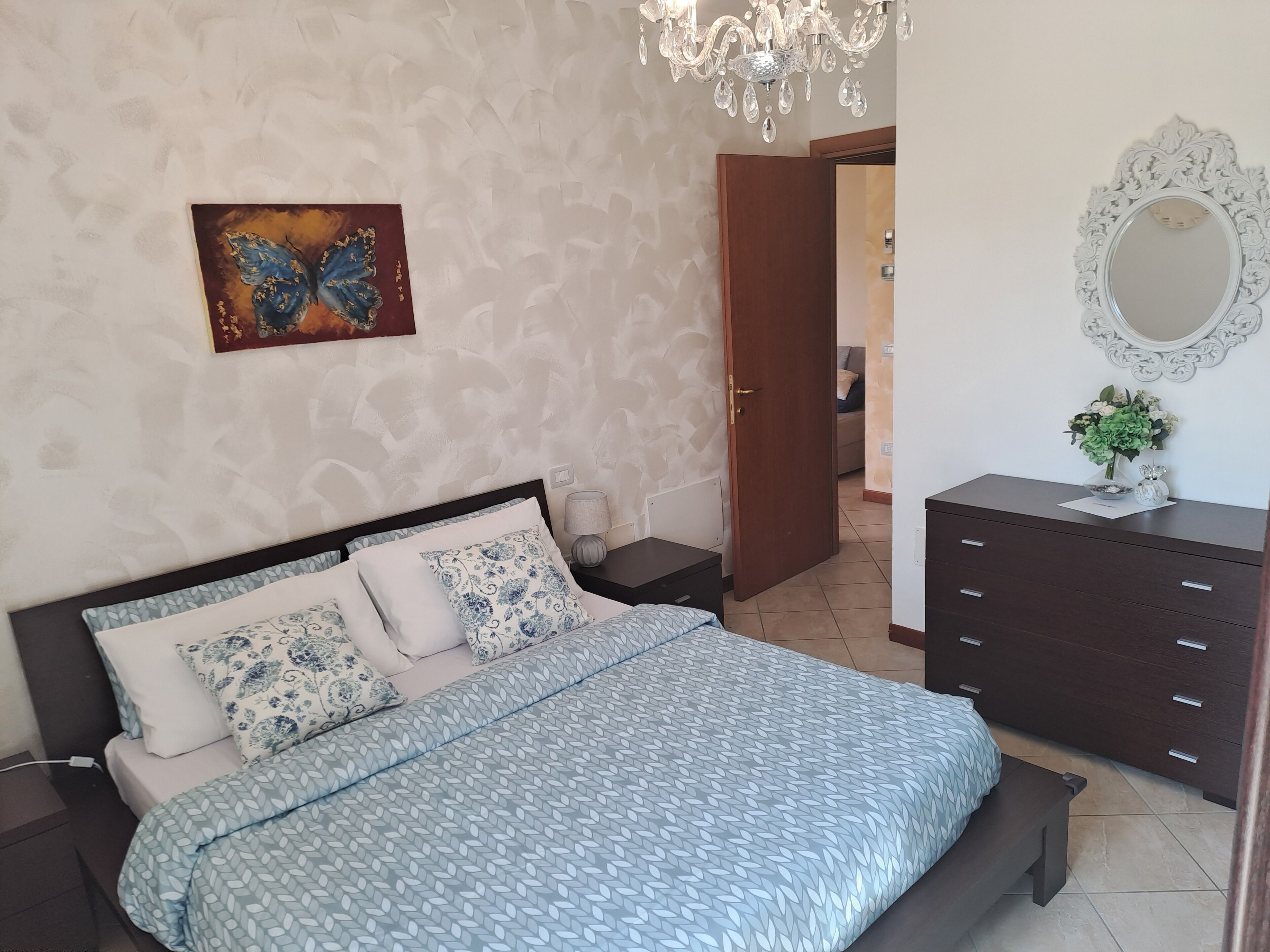Un dormitorio con cama, mesita de noche, cómoda, espejo y candelabro.
