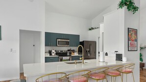 Una cocina moderna con una isla central, taburetes de bar y electrodomésticos de acero inoxidable.