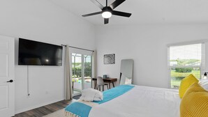 Habitación de hotel con cama, televisor de pantalla plana, ventilador de techo, escritorio con silla y vista a una piscina.