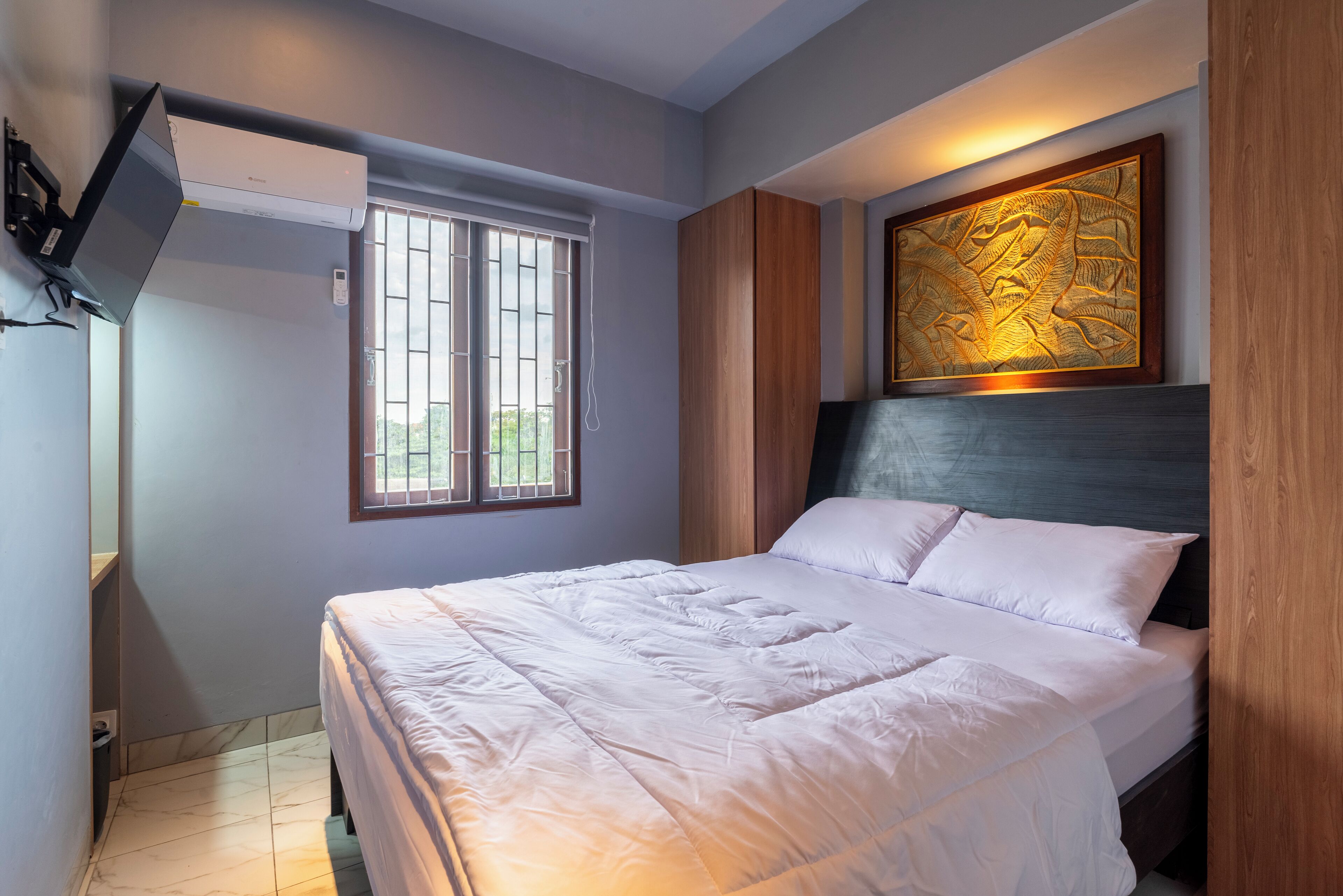 Une chambre à coucher avec un lit, une fenêtre, une œuvre d’art accrochée au mur et un ventilateur de plafond.