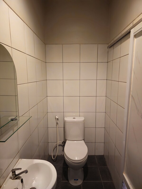Un baño pequeño y limpio con azulejos blancos, un inodoro blanco, un estante de vidrio y un lavabo con grifo.