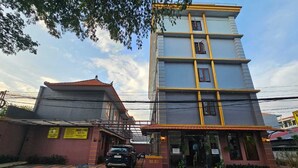 A multi-story hotel with a red-tiled roof, a red carpet entrance, and a parking area with a black car. - Hotel Dakozi Living (Kuta)