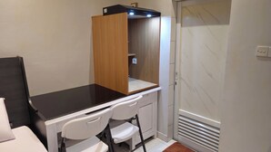 A compact room with a dark wooden desk, white chairs, a small white cabinet, and a door with a frosted glass panel. - Hotel Dakozi Living (Kuta)