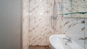 A bathroom with a white sink, a glass shower enclosure, and marble-patterned walls. - Hotel Dakozi Living (Kuta)