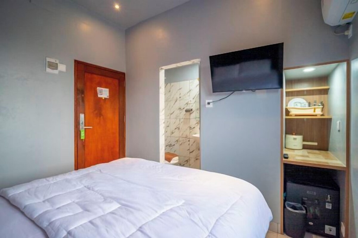 A hotel room with a bed, a television mounted on the wall, a wooden door, and a small bathroom visible through an open door.