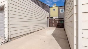 Une ruelle étroite, située entre deux bâtiments, avec un chemin en béton, une porte de garage sur la gauche et une petite fenêtre sur la droite.