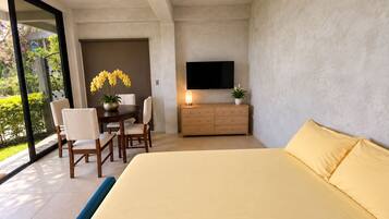 Un dormitorio moderno con una cama grande, televisión, zona de comedor con sillas y vistas a través de un ventanal.