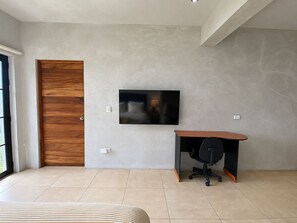 Een moderne slaapkamer met een groot bed, een houten deur, een flatscreen televisie aan de muur en een bureau met een stoel.