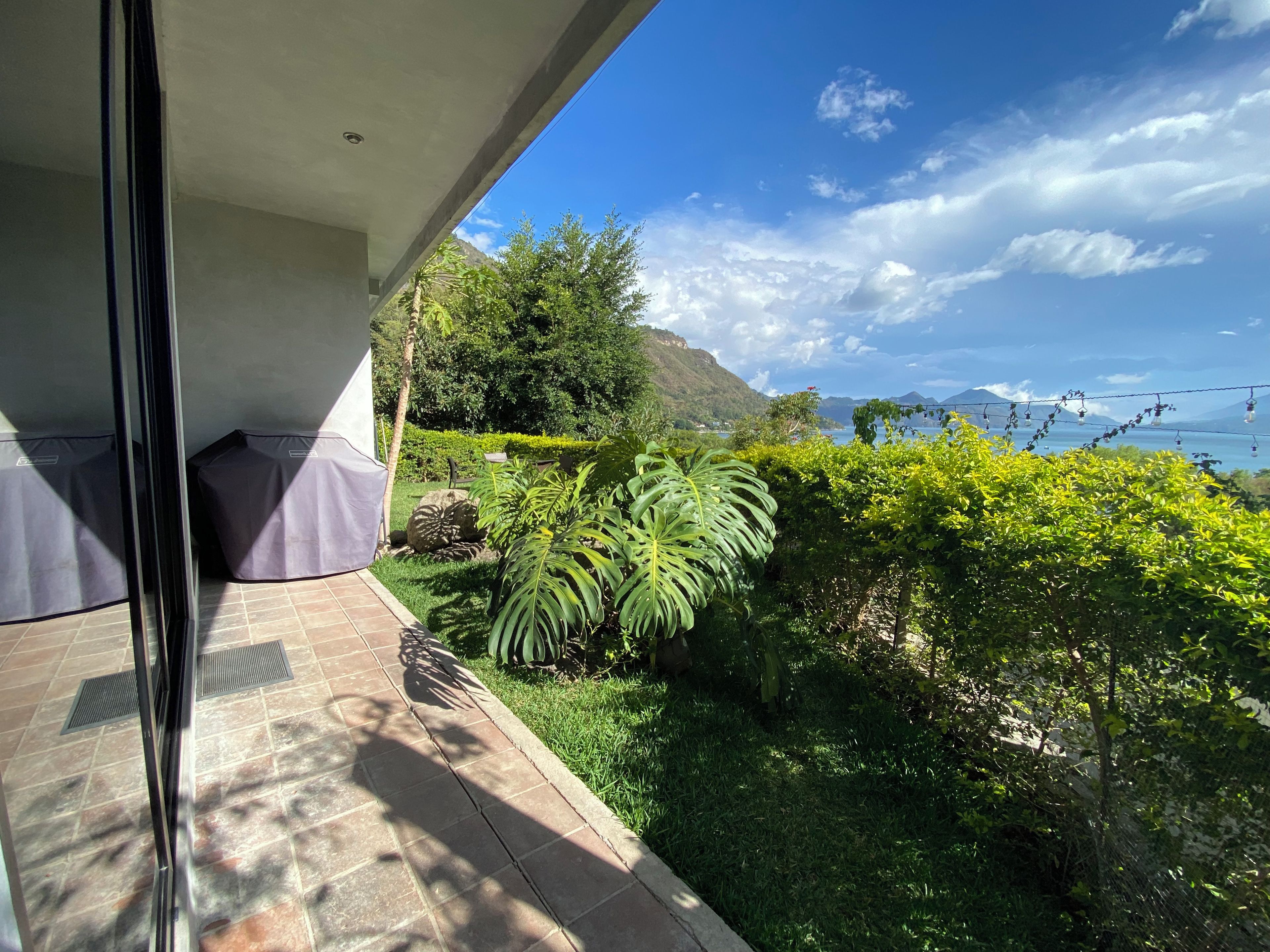 A balcony with a view of a lush garden and a distant mountain range.