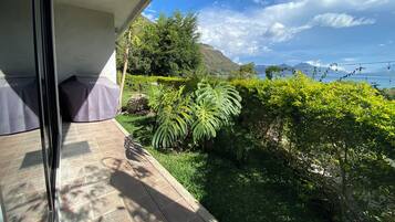 A balcony with a view of a lush garden and a distant mountain range.