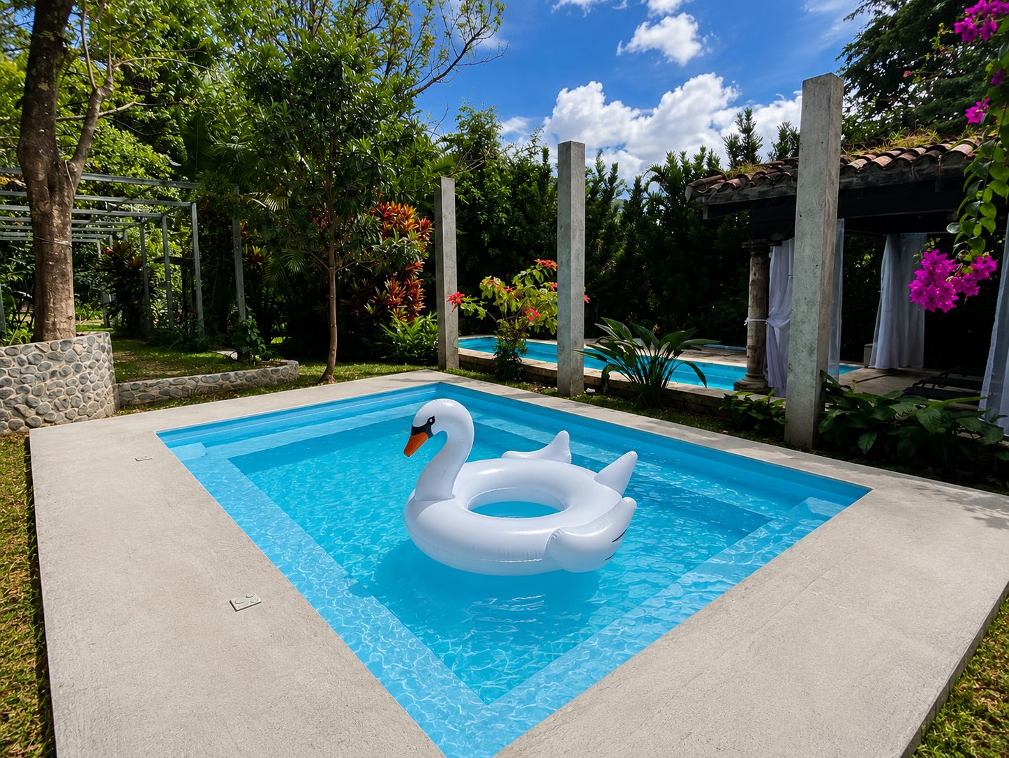 A swimming pool with a swan inflatable ring, surrounded by greenery and a clear sky.