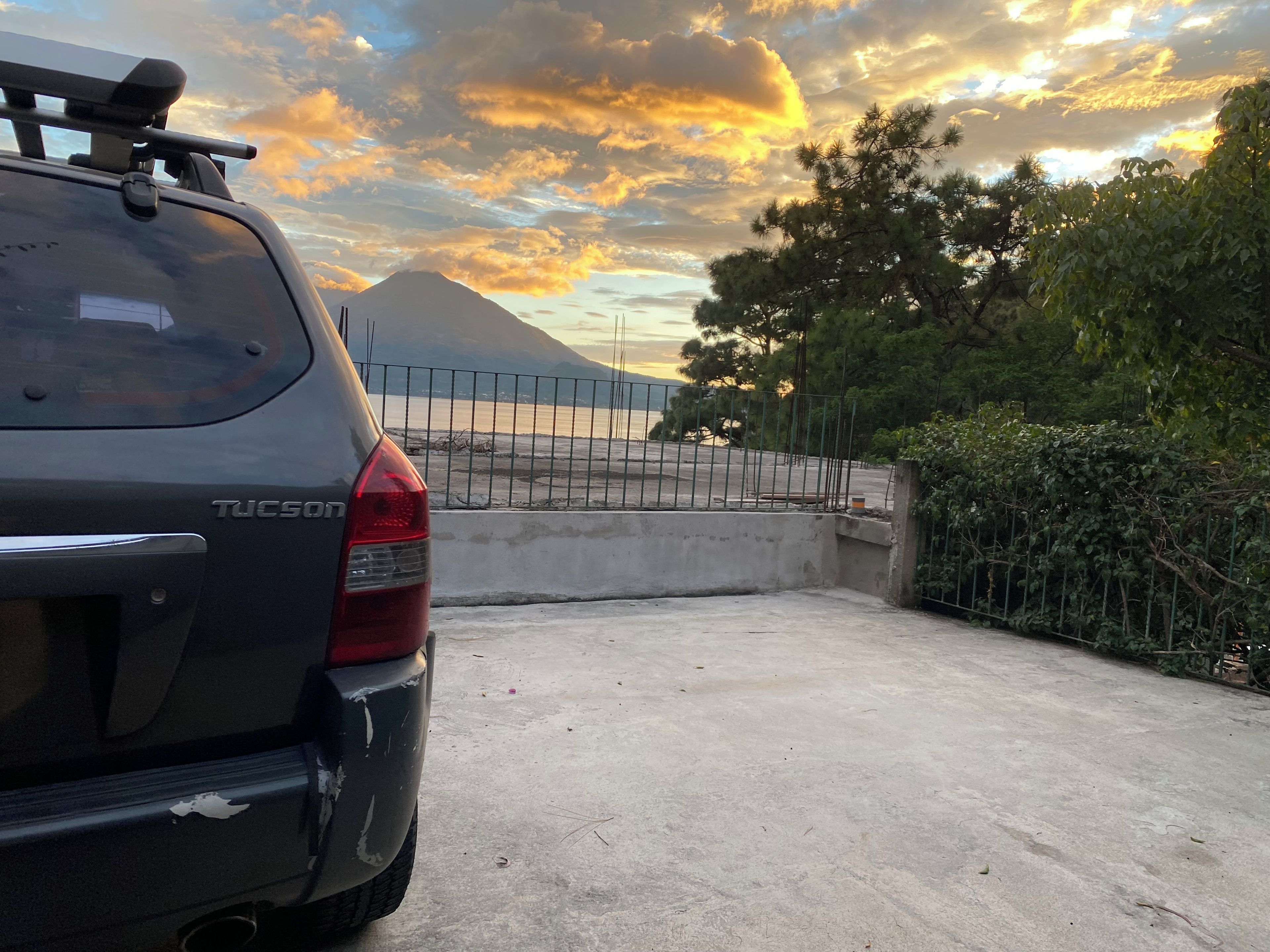 Un vehículo estacionado en un área de estacionamiento, con una montaña al fondo y una cerca en primer plano.