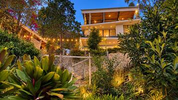 A modern two-story building with a stone retaining wall and lush greenery.