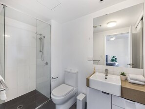 A modern bathroom with a glass-enclosed shower, a white toilet, and a sink with a mirror above it. - Steps to high end cafes and shops w/ Deck & pool (Fortitude Valley)