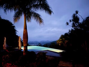 A swimming pool with a view of mountains, surrounded by palm trees and a wooden deck.