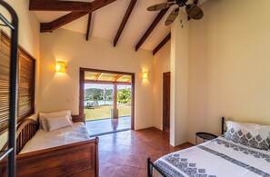 A bedroom with a bed, a window with blinds, a ceiling fan, and a view of a patio with a table and chairs.