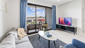 A modern living room with a sofa, a coffee table, a TV, and a balcony with curtains.