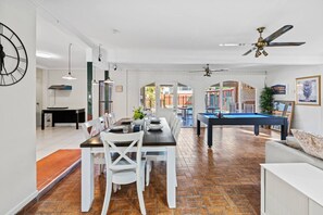 Amplia sala de estar con mesa de billar, comedor y mobiliario blanco.