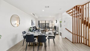 Un comedor moderno con una mesa preparada para cuatro personas, un sofá y una escalera con barandillas de madera.