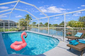 Ein Pool mit einem Flamingo-Schwimmsack, Liegestühlen und einer überdachten Liegefläche mit Blick auf Wasser und Palmen.