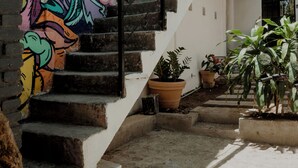 A staircase with a colorful mural on the wall, potted plants, and a white building with a metal staircase. - Sayula Home (Sayulita)