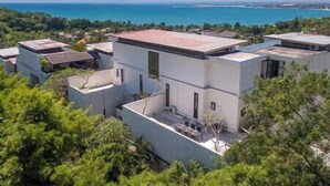 A modern residential complex with flat-roofed buildings, surrounded by greenery and overlooking a coastal area.