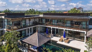 A modern multi-story house with a large balcony, a swimming pool, and a view of the surrounding landscape.
